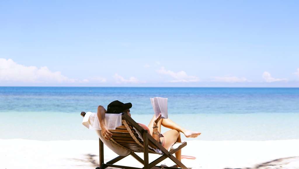 Pessoa relaxada em cadeira de praia, lendo um livro de frente para o mar